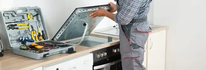 Cooktop repair technician lifting a built-in stovetop for service in Honolulu, HI