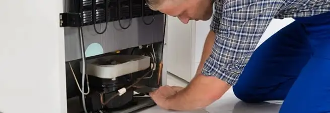 Refrigerator repair technician servicing the compressor and condenser area in Honolulu, HI