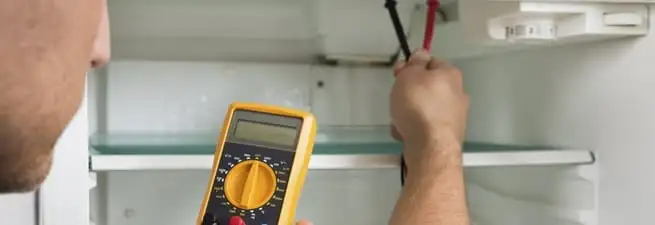 Refrigerator repair technician testing electrical components with a multimeter in Honolulu, HI
